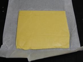 将原味面团放在一张长油纸的一侧，多余的油纸盖在面团上，用擀面杖擀成薄的长方形片。