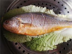 备一个蒸锅铺入菜叶子，把黄花鱼在上面，开大火蒸制，鱼肉泛白，鱼眼突出基本蒸熟。