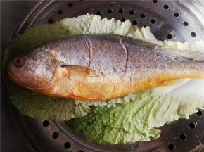 备一个蒸锅铺入菜叶子，把黄花鱼在上面，开大火蒸制，鱼肉泛白，鱼眼突出基本蒸熟。