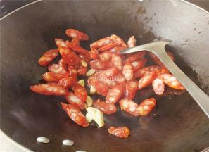 把蒜瓣，腊肠切片，热锅倒入少许食用油，把蒜片爆香，接着倒入腊肠片翻炒。