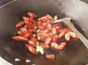 把蒜瓣，腊肠切片，热锅倒入少许食用油，把蒜片爆香，接着倒入腊肠片翻炒。