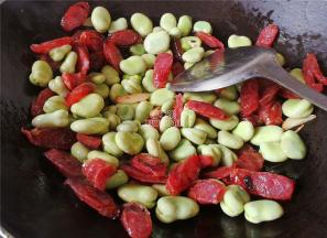 煸炒出腊肠油脂，把剥好的蚕豆洗净沥干倒入锅中一起翻炒。