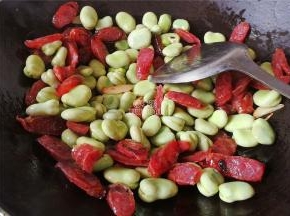 煸炒出腊肠油脂，把剥好的蚕豆洗净沥干倒入锅中一起翻炒。