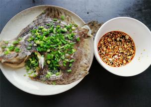 把多宝鱼从蒸锅里拿出来，倒掉盘中多出来的水分，撒入切好葱花，把料汁也淋入鱼面。