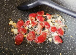 锅中再倒入少许油，放入切好的蒜瓣爆香，把腊肠片放入煎出油脂。