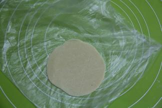 酥皮也分12份，25克一份。放在保鲜袋一侧，然后保鲜袋对折，用擀面杖轻轻擀成圆形。