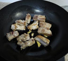 排骨煎至两面金黄后加入姜片和大蒜，继续翻炒几下。