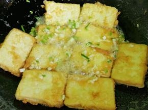 炸豆腐的油倒出一些来，留一点底油，把所有炸好的豆腐都放进锅里，放入葱花和蒜末。