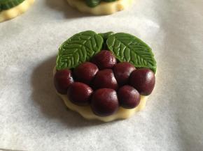 再将红曲面团揉成长细条状，切成若干小团子，依次揉圆放置在叶子下方，一串葡萄就完成了；