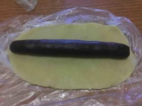 将大的那份原味面团擀成薄片，再将可可粉面团滚圆成薄片长度，放置其上；