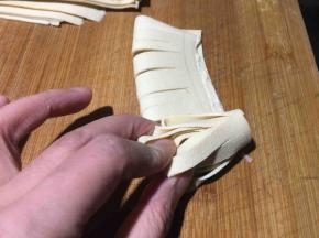 然后左手按住细条，右手大拇指和食指将对折齐边从下往上卷起来；