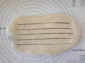 将包好内陷的面团擀成椭圆形，用刀在表面划出4-5道口