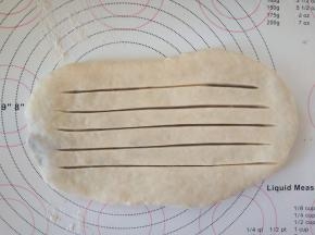 将包好内陷的面团擀成椭圆形，用刀在表面划出4-5道口