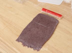 松弛好的面团用擀面杖擀成长方形面团，宽度和蟹柳长度相当。底端用手指压扁，这样待会好粘合。