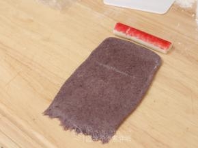 松弛好的面团用擀面杖擀成长方形面团，宽度和蟹柳长度相当。底端用手指压扁，这样待会好粘合。