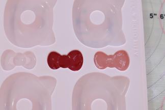 用白巧克力加入少需的红色色素，调成粉色巧克力液，做好蝴蝶结，大红巧克力液做好大红蝴蝶结，放入冰箱冷藏定型。