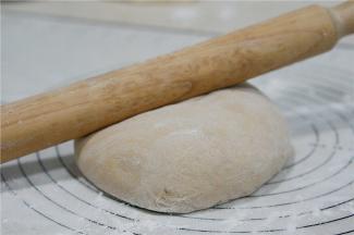 用擀面棒将面团擀至方长薄面皮状。