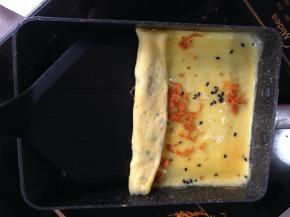 蛋液还没有凝固时撒少许黑芝麻和肉松，从一边慢慢用铲子卷起，卷紧