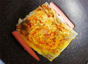 把鸡蛋面翻过来，涂抹上蒜蓉辣酱，香肠切半放锅中煎制下。