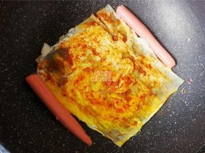 把鸡蛋面翻过来，涂抹上蒜蓉辣酱，香肠切半放锅中煎制下。