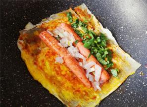 最后把香肠放入面皮上，撒入洋葱碎，香菜，白砂糖，浇入点陈醋，卷起来锅铲分割成小块即可。