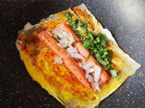 最后把香肠放入面皮上，撒入洋葱碎，香菜，白砂糖，浇入点陈醋，卷起来锅铲分割成小块即可。