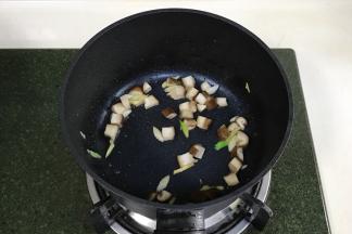 开火，锅中加入少许食用油，加入蘑菇丁炒至变色，加葱姜翻炒片刻。