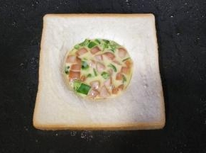 用勺子将植物蛋香肠青椒混合物放在吐司圆孔里，煎至植物蛋液底部成形