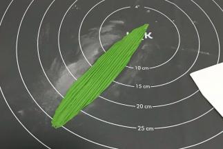 从绿色面团中分隔一点小面图出来，搓成椭圆形，硅胶垫上撒粉防粘，用擀面杖擀长。用刮板压出条纹，成粽叶的纹路。