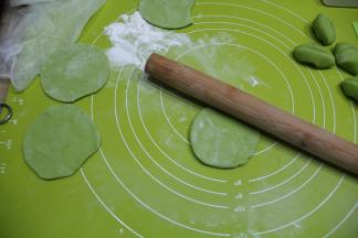 揉面垫略洒粉，取一个小面团，略规整圆，然后掌心按压扁一点，左手捏住左下边，右手拿擀面杖向左倾斜45℃角，由外往里推薄饺子皮，右手一边推，左手要逆时针转动面皮，让面皮的四周都要擀到，擀薄，成中空略厚，四周薄的圆形皮。