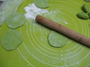 揉面垫略洒粉，取一个小面团，略规整圆，然后掌心按压扁一点，左手捏住左下边，右手拿擀面杖向左倾斜45℃角，由外往里推薄饺子皮，右手一边推，左手要逆时针转动面皮，让面皮的四周都要擀到，擀薄，成中空略厚，四周薄的圆形皮。