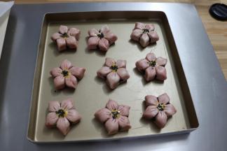 放烤盘里，在每个花蕊中心用毛笔刷蛋液，撒黑芝麻