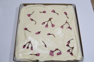 从20厘米高处慢慢倒入铺好油纸的烤盘上。晃动烤盘，让蛋糕糊晃平，或者用刮板刮平，快速摆入处理好的樱花，摆均匀一些。提起轻震一下烤盘。