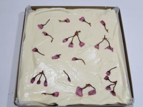 从20厘米高处慢慢倒入铺好油纸的烤盘上。晃动烤盘，让蛋糕糊晃平，或者用刮板刮平，快速摆入处理好的樱花，摆均匀一些。提起轻震一下烤盘。