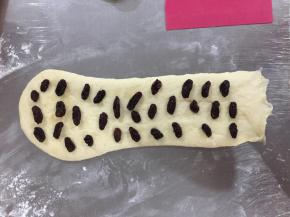 松弛好的面团再次擀成长条，放上葡萄干。