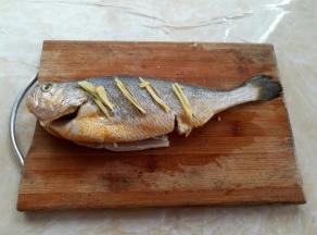 黄花鱼去鳞、去内脏和鱼鳃，鱼肚子和鱼嘴巴里黑色的内膜撕掉，黄花鱼的正反两面鱼身上划4刀，先在鱼身、鱼肚和鱼头里抹适量的盐，简单入味，然后放上适量的姜丝和葱白去腥