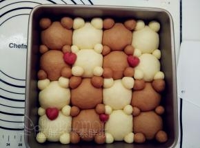 取出发酵好的面团，在情侣熊的耳朵和手脚后面蘸一点水，摆在相应的位置上。红色小剂子整合成爱心造型，摆放在相应位置。