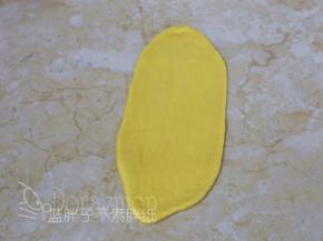 松弛好的面团压扁，用擀面杖擀成椭圆形。