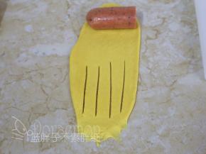将面团翻面，顶端摆上半根香肠，下端用手指压扁，偏下的位置用刀划出四道口。