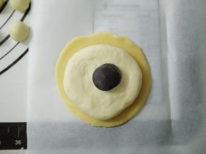 放上一个压扁的面团，在放巧克力，将面团收口包住馅料，同时将酥皮收拢包住面团。