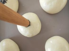 12、发酵结束后面团表面涂全蛋液，用擀面杖一头沾水，再蘸芝麻，轻轻压在面团中间。