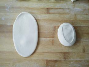 取一个面团切面朝上，用手按压，用擀面杖擀成牛舌状。