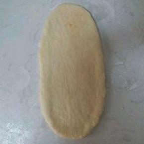 包好的面团再按扁，用擀面棍轻轻擀制长椭圆形