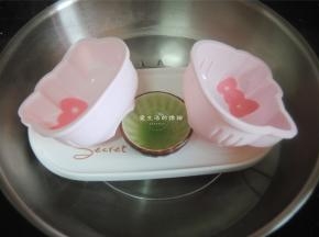 将学厨4寸KT硅胶模具放入煮沸水的锅里，倾斜角度，将粉色的马蹄浆用勺子放在蝴蝶结处，盖好盖子，蒸2分钟凝固。