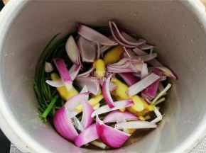 备一个高压锅，小葱铺入底部，分别放入姜片，洋葱块还有大块冰糖。