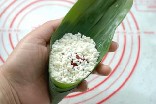 然后放入一半浸泡好的圆粒糯米，再放入一颗大枣，再放上一层糯米，糯米放九分满就好了，不要太多，留一分给糯米一个膨胀的空间，糯米煮熟后还会胀大。米放得太多不仅容易漏米，而且，不容易包的住。但也不能太少，米太少煮熟后会发散，粘合不到一起，口感也不好，九分满是最好的。