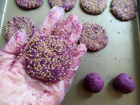 把紫薯面团放手心里按扁，两面沾上适量的白芝麻放到烤盘里，间隔出一定的位置