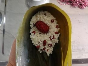 左手抓托住折好的粽叶，舀入一大勺糯米，铺在底部，放入红枣。