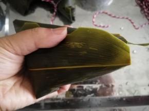 右手帮忙。把两边的粽叶往下压好，成三角状。