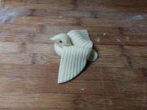 再捏出小鸟嘴，两边各按下一粒黑豆做小鸟眼睛